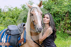 Charming young sexy woman slim body in black dress standing with brown horse on nature background. Face of portrait lady long