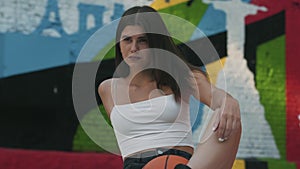 Charming young tanned sportswoman resting on outdoor court after basketball playing training. Portrait of confident fit