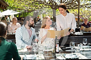 Charming young waiter and couple at open-air restaurant summer