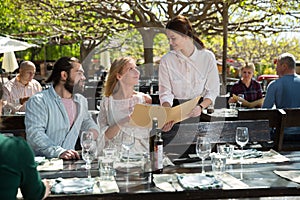 Charming young waiter and couple at open-air restaurant summer