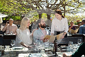 Charming young waiter and couple at open-air restaurant summer