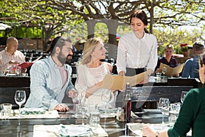 Charming young waiter and couple at open-air restaurant summer