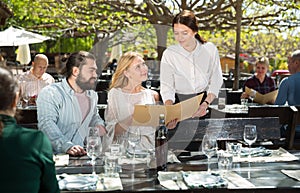 Charming young waiter and couple at open-air restaurant summer