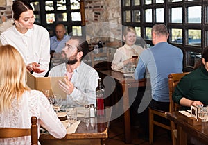 Charming young waiter receiving order from guests in country restaurant