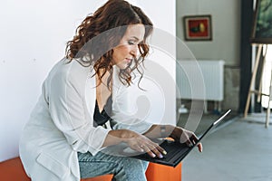 Charming young woman business lady in white suit using laptop in the modern art gallery