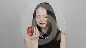 Charming young woman eats a red apple and smiles