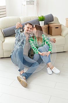 Charming young woman kisses her husband holding in hands the keys to their new apartment while sitting in her new living