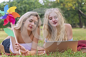 Charming young woman lying on mat with her friends holding windmill in her hands while looking at laptop. Joyful two teenagers