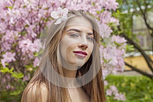 Charming young woman with natural makeup and healthy long brown hair in blossom park outdoors. Natural female beauty portrait