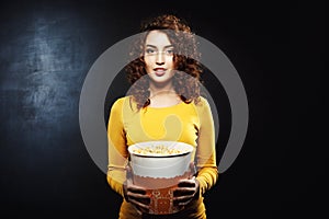 Charming young woman with popcorn bucket isolated on black background