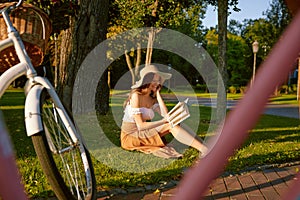 Charming young woman reading book while sitting in park