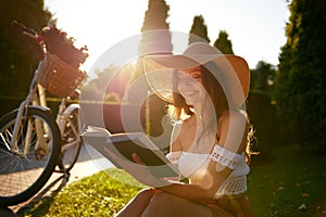 Charming young woman reading book while sitting on park bench in sunlight beam