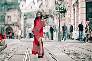 Charming young woman in red sexy dress posing with a bouquet of red roses. photo of a seductive woman with black hair on