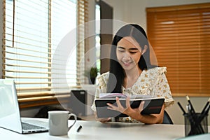 Charming young woman sitting at desk in home office and checking her working schedule plan