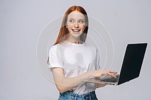 Charming young woman student holding laptop computer and looking away on isolated gray background