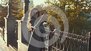 Charming young woman in sunglasses walks through autumn city in coat in slomo