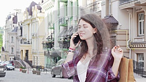 Charming young woman talking on the phone on city street holding shopping bags