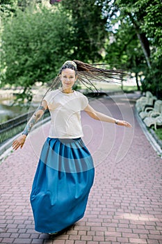 Charming young woman in white t-shirt and blue skirt, with dreadlocks hair style, walking and dancing in the park