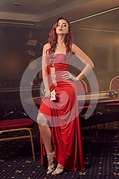 Charnimg sexy woman is posing against a poker table in luxury casino.