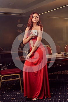 Charnimg sexy woman is posing against a poker table in luxury casino.