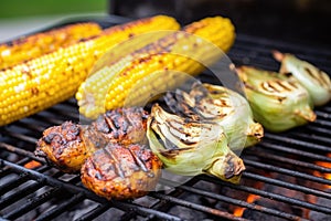 charred corn on the cob next to bbq burgers on a grill