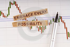 On the chart of business quotes lies a pen and torn paper with the inscription - Embrace Every Possibility