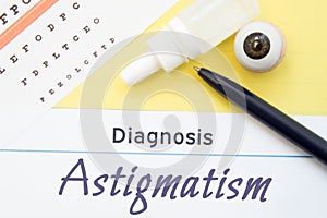 Chart for testing visual acuity, eye drops and eye anatomical model lies next to inscription Diagnosis Astigmatism. Concept for di