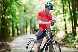 Chatting in internet. Cyclist on a bike is on the asphalt road in the forest at sunny day