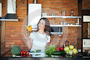 Chatty brunette woman playing with vegetables while talking on mobile phone on her modern kitchen