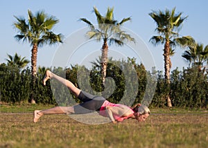Chaturanga pose with one leg up. Fit caucasian woman do yoga or push up on the grass outdoor in vacation, selective