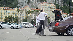 Chauffer helping young woman with luggage, elite car service, transportation