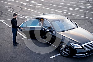 Chauffeur helps a businesswoman to get out of a car on parking lot