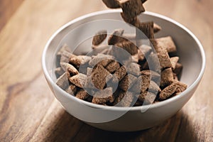 Chcolate cereal pillow falling into white bowl on table