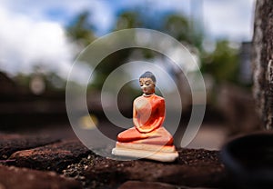 Cheap clay figurine of Buddha left on an old brick wall