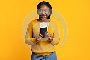 Cheap Flights. Excited Black Lady Holding Passport And Tickets On Yellow Background