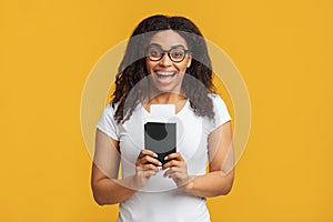 Cheap flights. Overjoyed black lady holding passport and tickets, standing over yellow background