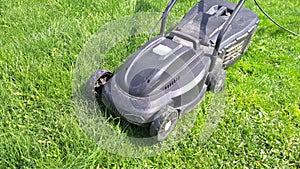 cheap plastic electrical lawn mover on green lawn at sunny day