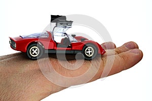 Cheap red plastic model of street-legal vintage racing car with opened gullwing doors, held in on back of hand of adult man.