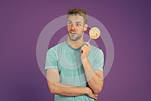 Cheat meal concept. Sugar harmful for health. Guy hold lollipop candy violet background. Man handsome macho eat big