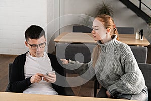 Cheater man dating on line with a smart phone and girlfriend is spying sitting on a sofa in the cafe photo