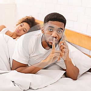 Cheating african husband talking privately on cellphone in family bed