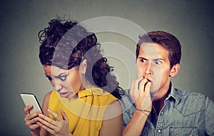Cheating boyfriend. Man nervously biting fingernails while shocked girlfriend reading text messages on his mobile phone