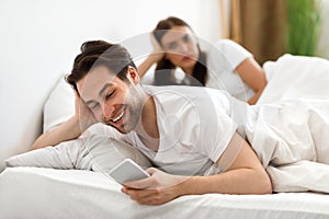 Cheating Husband Texting On Phone Ignoring Wife Lying In Bed photo