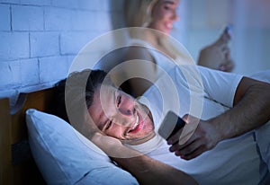 Cheating Husband Texting On Phone Lying With Wife In Bedroom