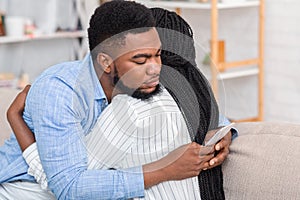 Cheating husband texting with somebody on cellphone while embracing his wife