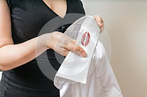 Cheating and infidelity concept. Woman holds white shirt of her husband with red lipstick stains. photo