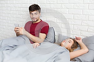 Cheating man with smartphone texting message in bed