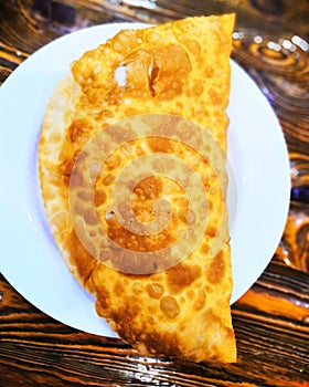 Cheburek on a round plate on a wooden table