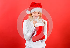 Check contents of christmas stocking what she received. Woman in santa hat unpacking christmas gift red background