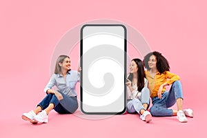 Check this offer. Happy diverse female friends sitting near huge smartphone with blank screen, mockup